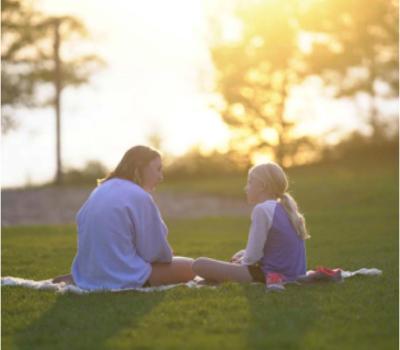 Two girls sitting on blanket in field